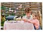 Dve deti pripravujú hračkársku pizzu vo vonkajšej peci na pruhovanom obruse.