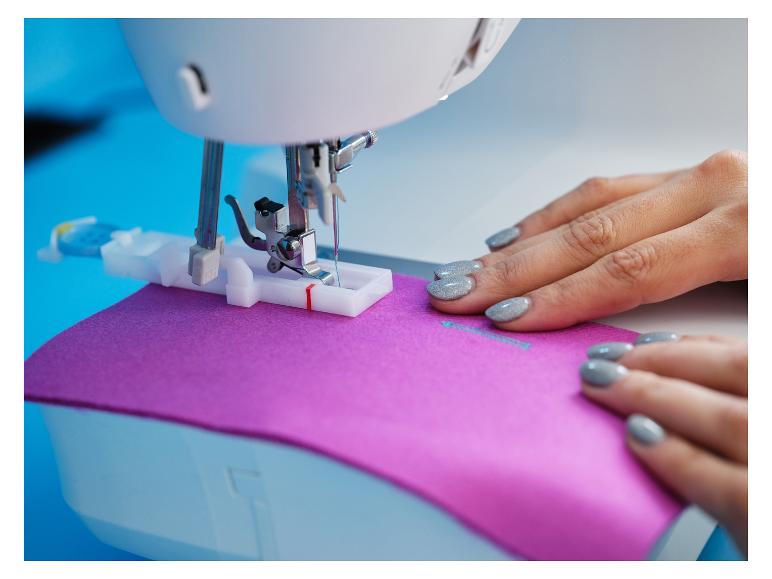 Žena šije fialovú látku na šijacom stroji.