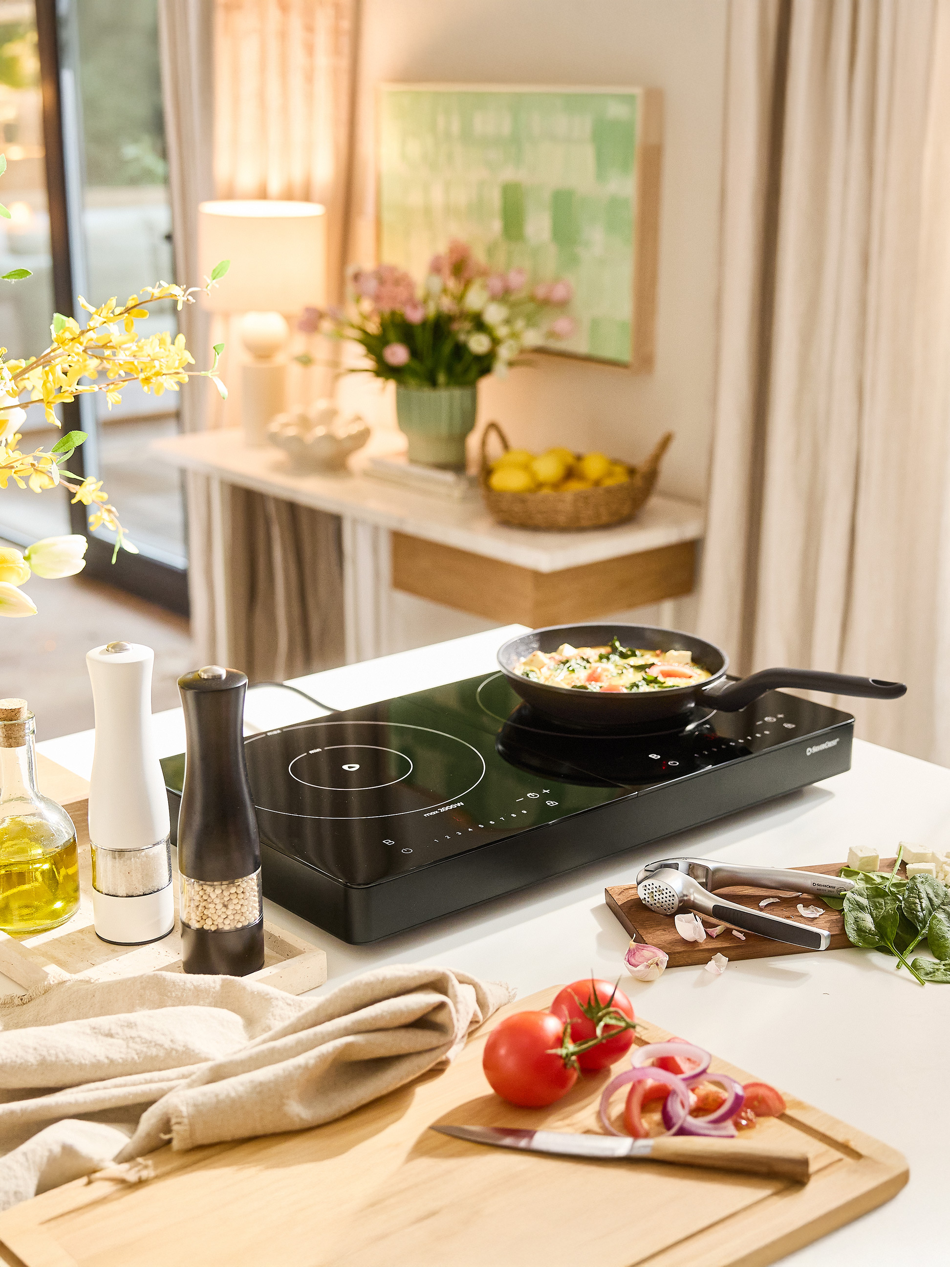 Indukčná varná doska SilverCrest s panvicou, korením a čerstvou zeleninou na kuchynskej linke.