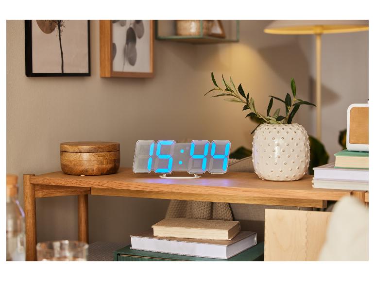 Digitálne LED hodiny, knihy a ozdobná váza na drevenom nábytku.