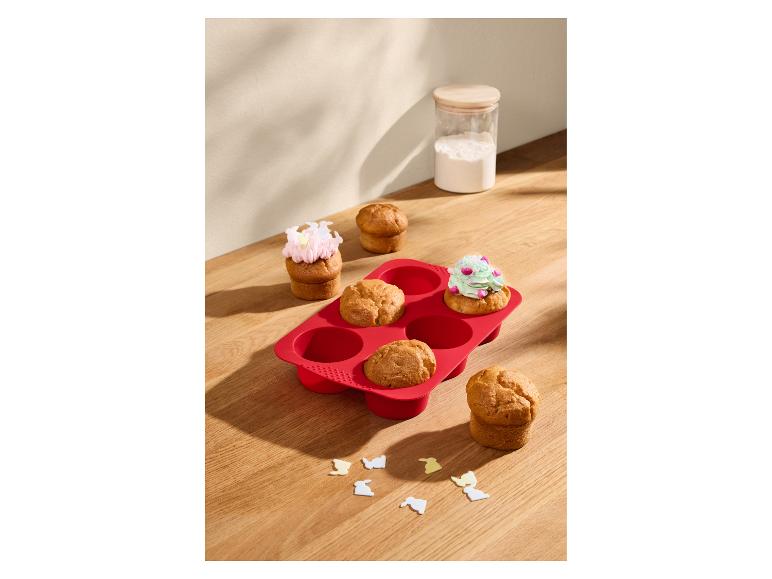 Červená silikónová forma na muffiny s upečenými muffinmi, niektoré zdobené polevou.