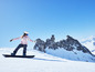 Snowboarder v ružovom oblečení a modrých okuliaroch ide na snowboarde po zasneženom svahu.