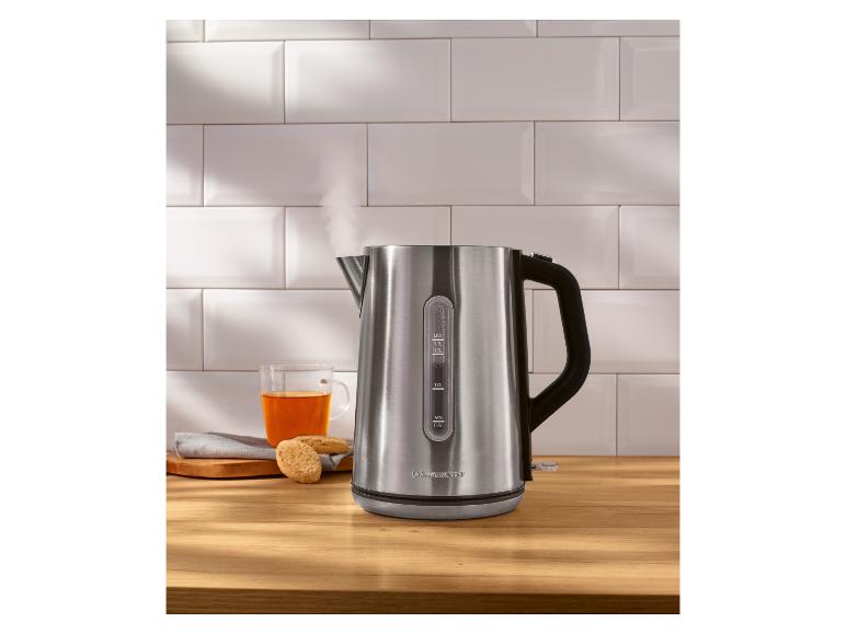 Nerezová rýchlovarná kanvica s parou, vedľa šálky čaju a sušienok.