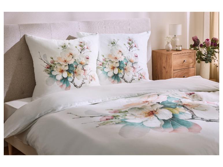 Posteľ s bielou posteľnou bielizňou s kvetinovým vzorom a ladiacimi vankúšmi.