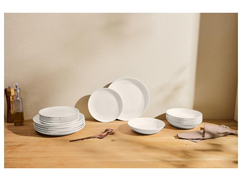 Súprava bieleho riadu na drevenom stole s fľašami oleja a korenia.