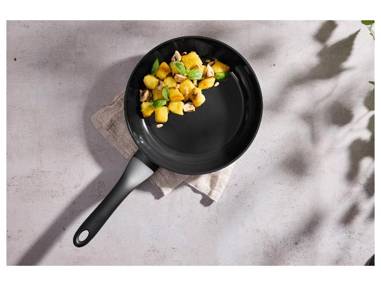 Panvica s opekanými zemiakmi, hubami a bazalkou na svetlom pozadí.