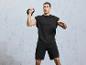 Muž v čiernom tričku a šortkách cvičí s kettlebell.