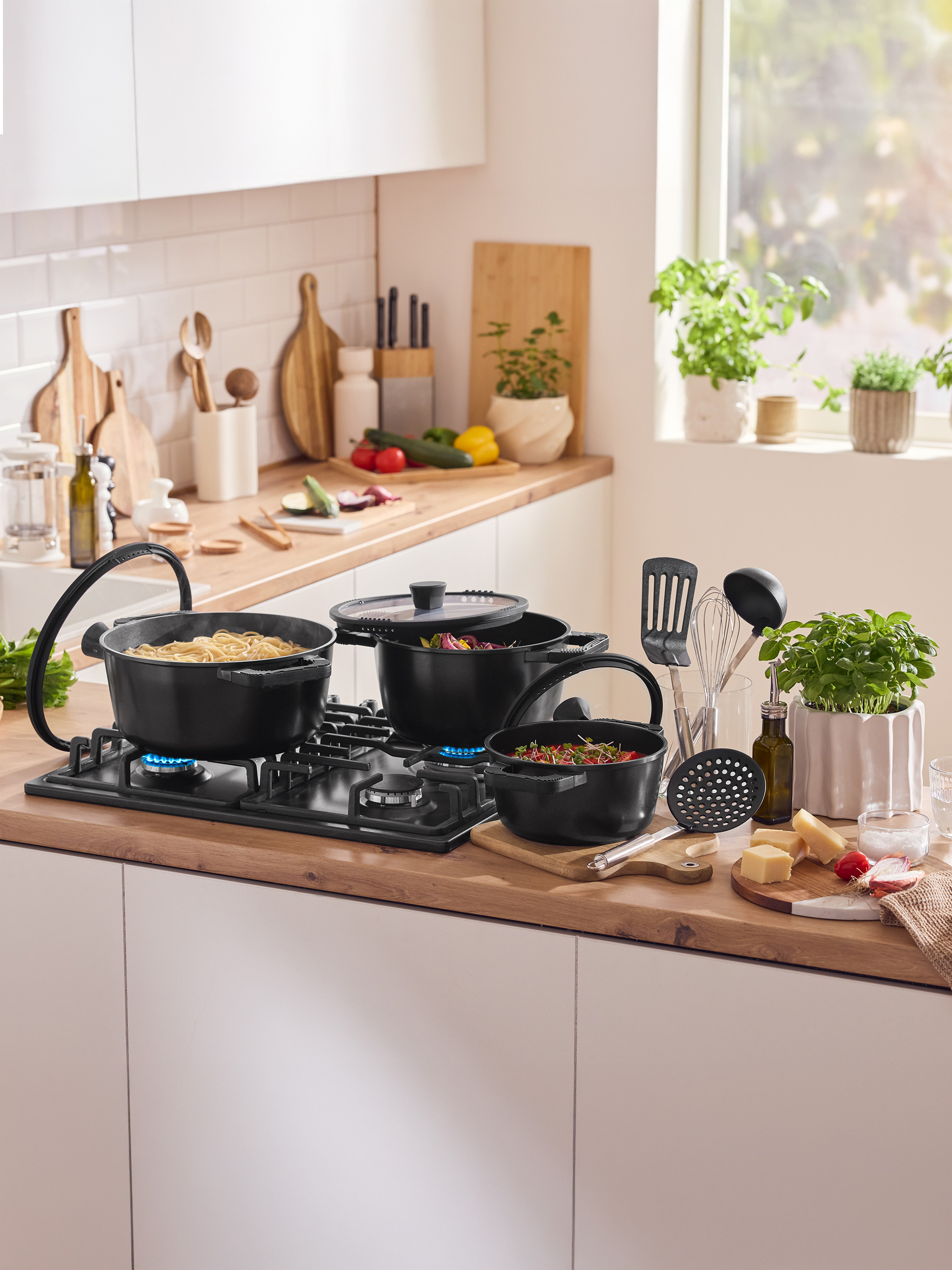 Kuchynská linka s hrncami na sporáku, kuchynskými pomôckami a čerstvými prísadami.