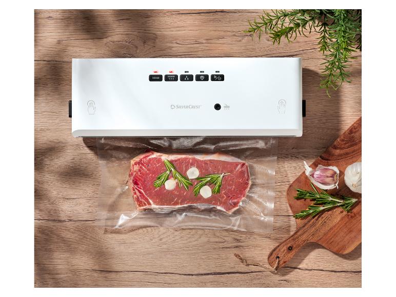 Vákuová zváračka SilverCrest so steakom, rozmarínom a cesnakom na drevenom stole.
