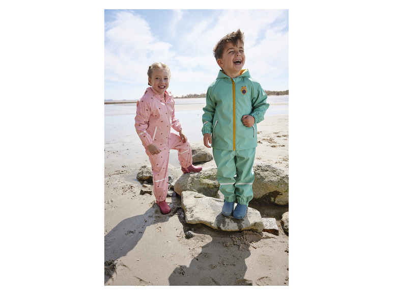 Dve deti v dažďovom oblečení na pláži.