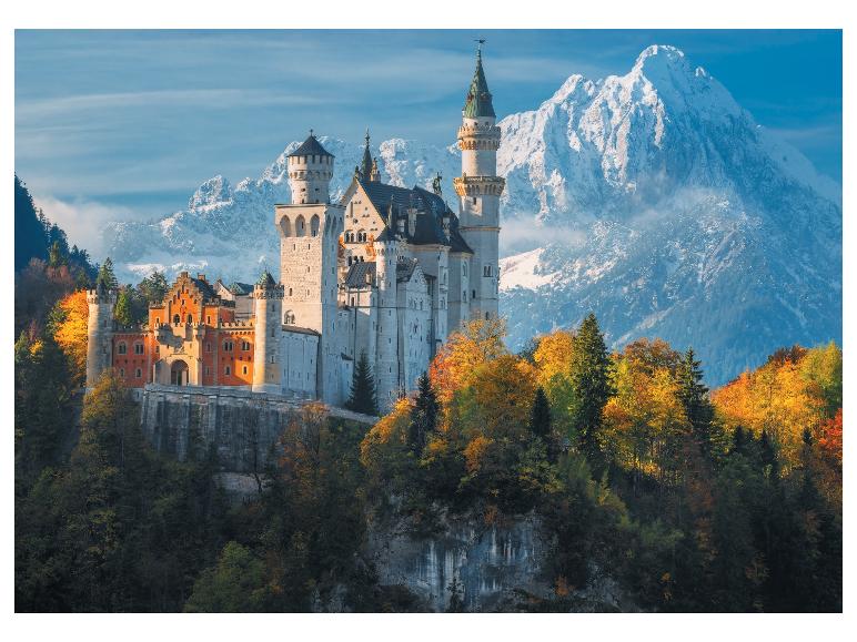 Hrad Neuschwanstein, obklopený jesennými stromami a zasneženými horami.