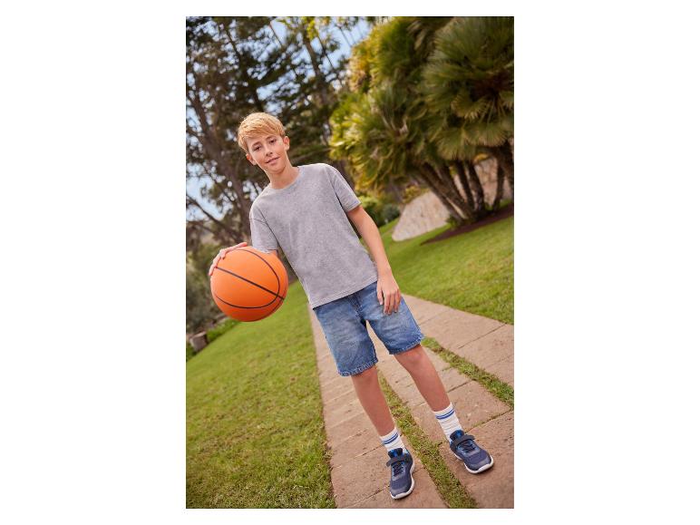 Chlapec v sivom tričku a džínsových šortkách drží basketbalovú loptu na chodníku.