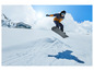 Snowboarder v modrej bunde a čiernej prilbe skáče nad snehom.