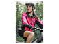 Žena v ružovej cyklistickej bunde a čiernej prilbe na horskom bicykli.