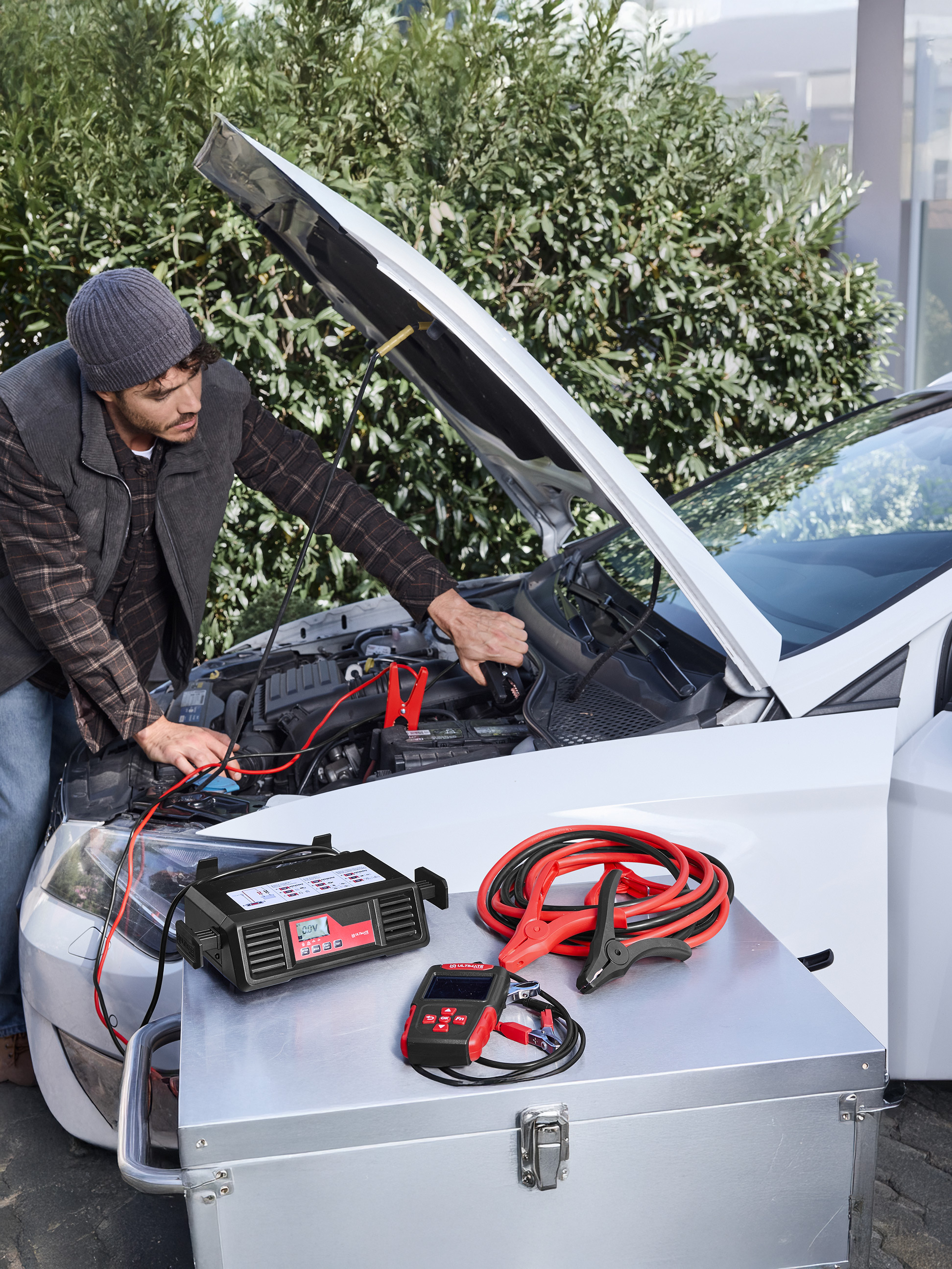 Muž používa nabíjačku do auta ULTIMATE SPEED a štartovacie káble na aute.