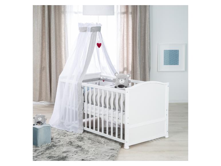 Biela detská postieľka s baldachýnom, sivým plyšovým medvedíkom a kobercom v detskej izbe.