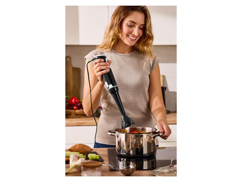 Žena používa ponorný mixér v hrnci so zeleninou na varnej doske.