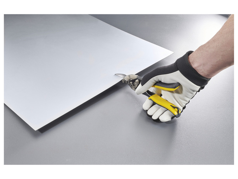 Ruka s žltými nožnicami na plech strihá plech.