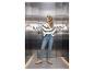 Žena v džínsoch a pruhovanom svetri stojí vo výťahu s rukami na stenách.