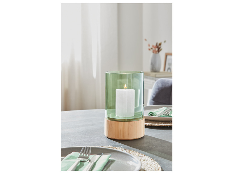 Zelená sklenená sviečka v drevenom stojane.