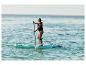 Žena pádluje na paddleboarde v mori, oblečená v záchrannej veste.