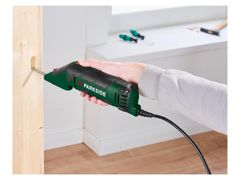 Ruka drží elektrické dláto, ktoré vyrezáva otvor do dreveného trámu.