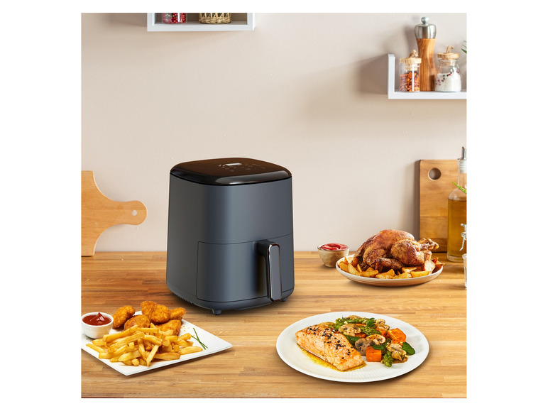 Airfryer s vyprážaným kurčaťom, hranolkami a lososom na drevenom stole.