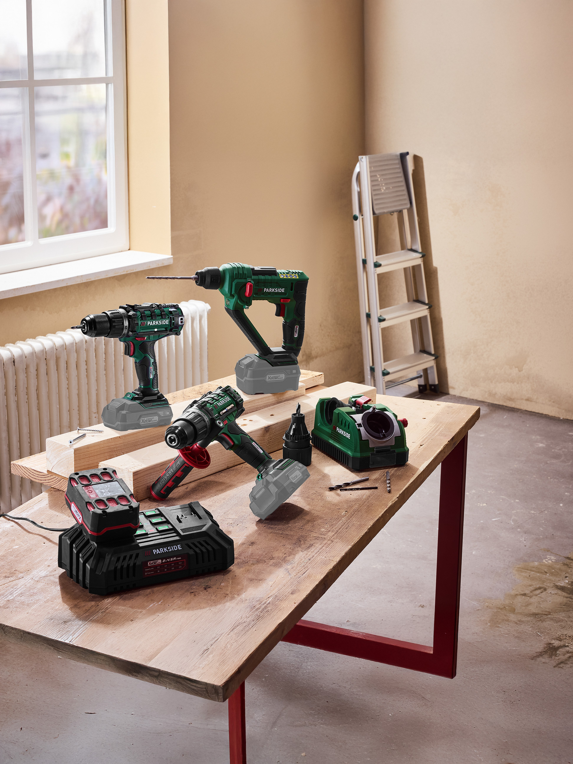 Elektrické náradie vrátane vŕtačiek a nabíjačky batérií na drevenom stole.