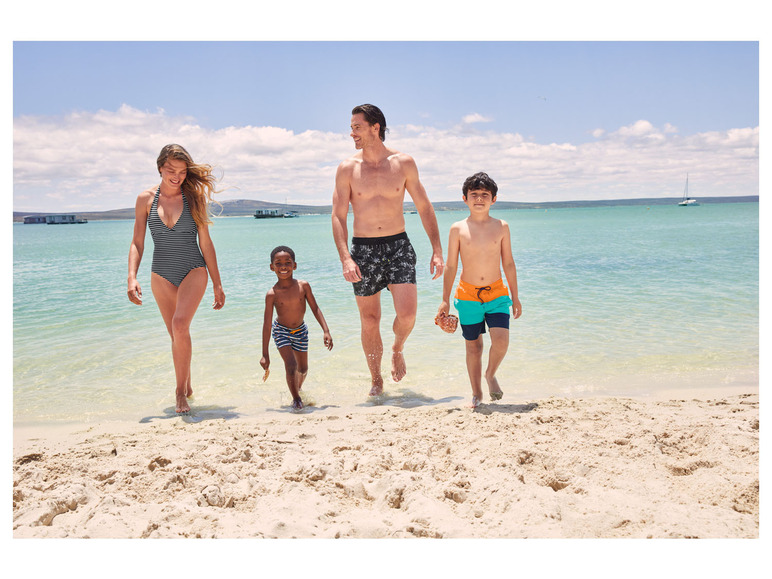 Rodina v plavkách kráča po piesočnatej pláži.