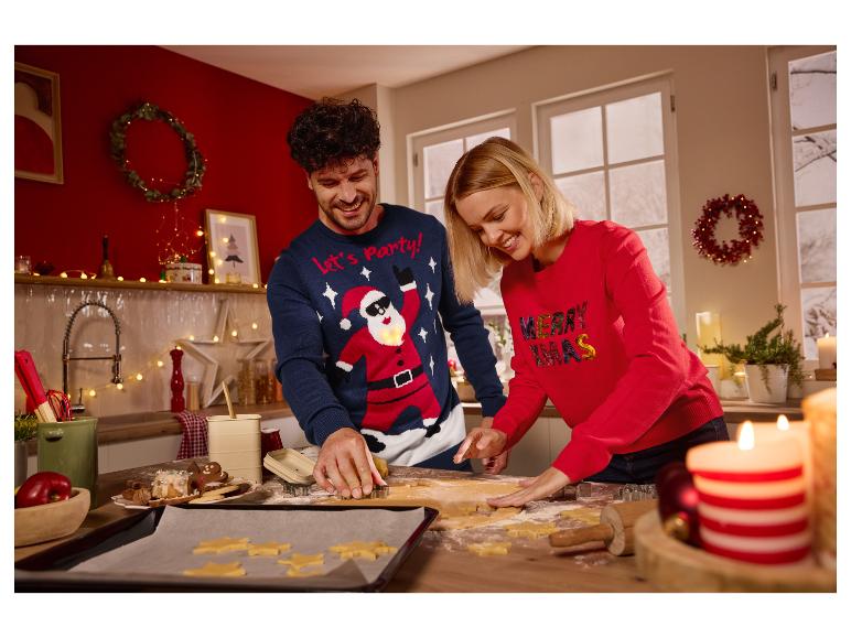 Usmiaty pár vianočných svetrov krája sušienky v kuchyni.