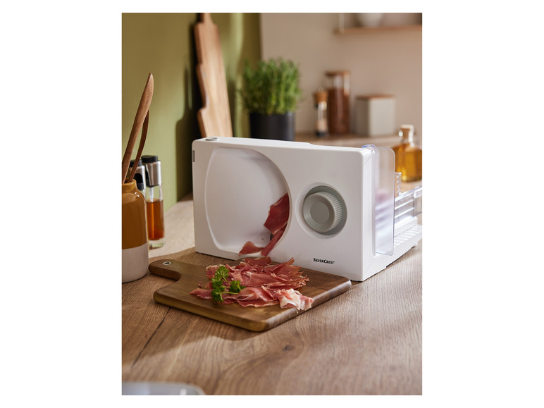 Biely krájač Silvercrest krája prosciutto na drevenej doske.