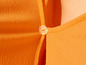 Detail oranžového trička s gombíkom.