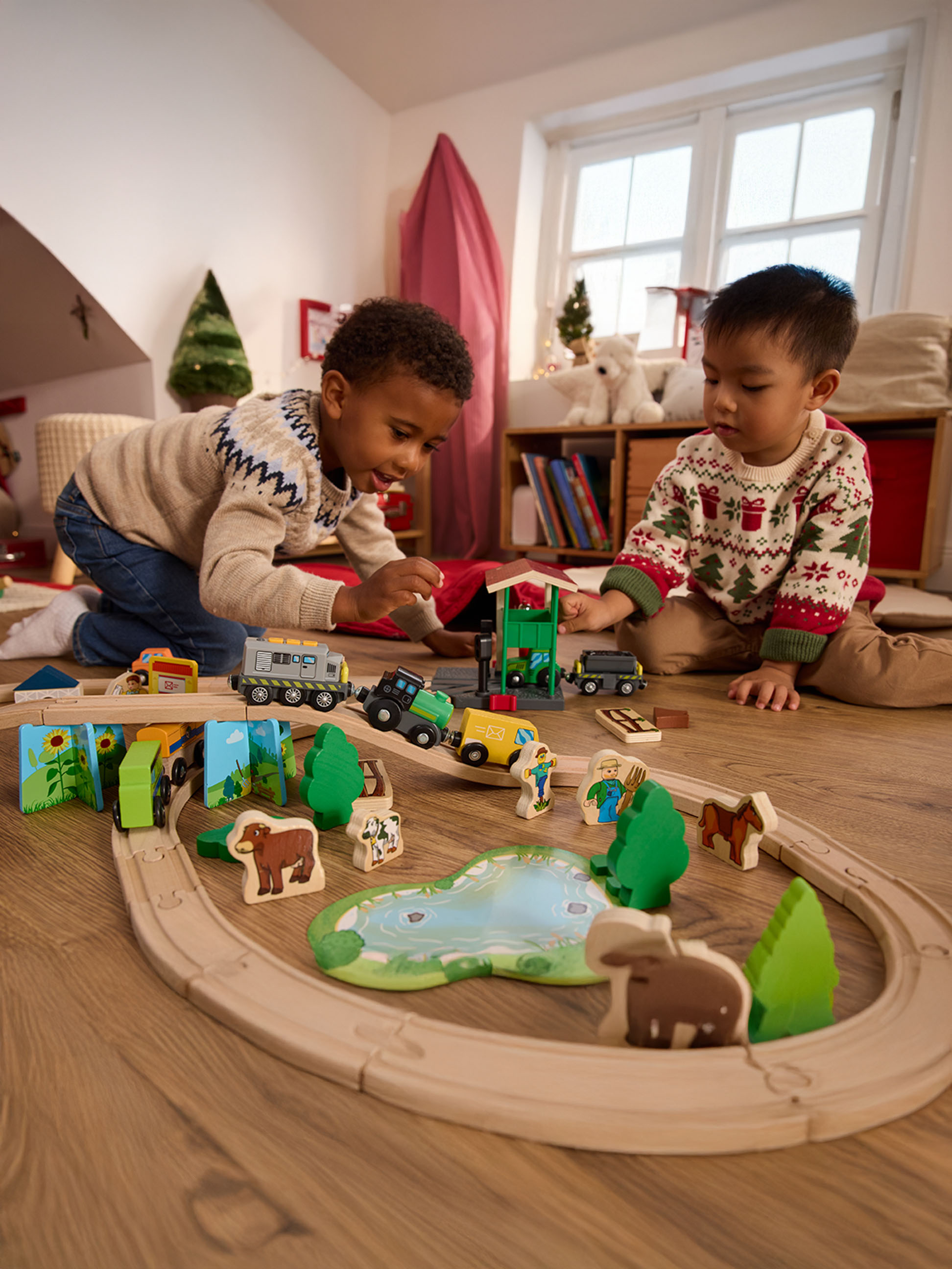 Dvaja chlapci sa hrajú s dreveným vláčikom a figúrkami zvierat na drevenej podlahe.