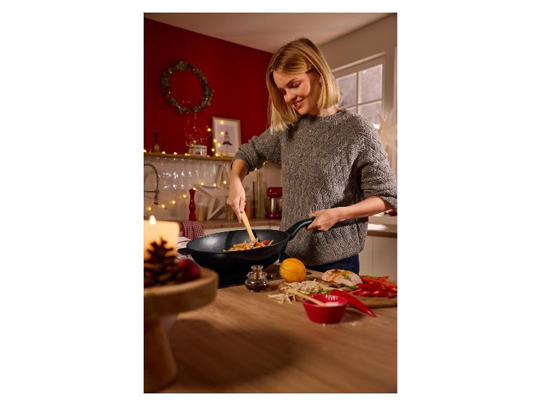 Usmievavá žena varí stir-fry vo woku, s čerstvými prísadami na pulte.