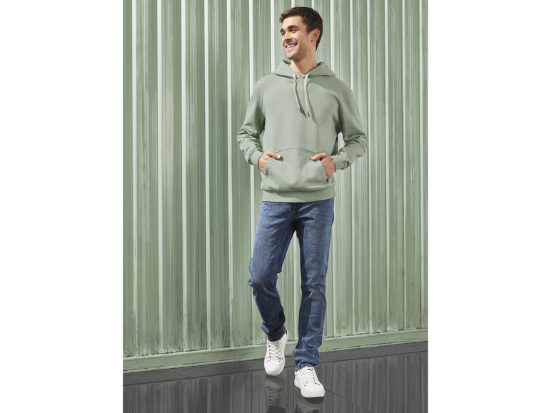 Muž v zelenej mikine a modrých džínsoch.