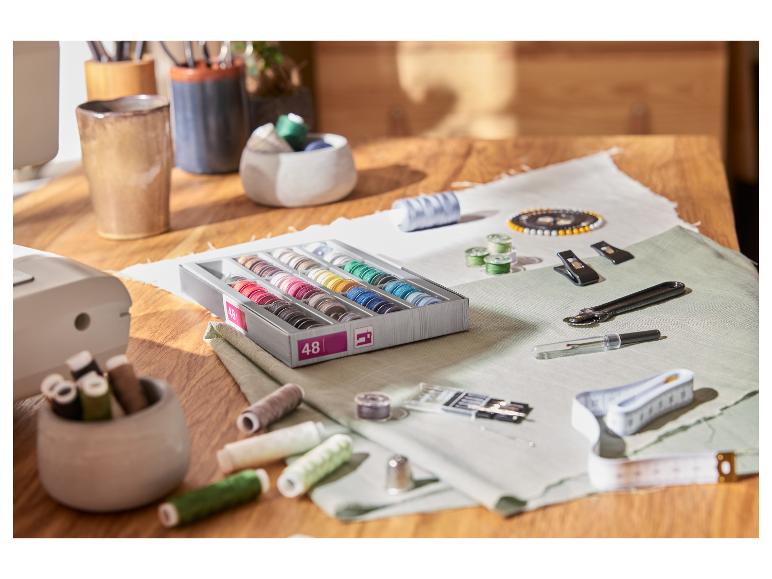 Šijacie potreby na drevenom stole: krabica s 48 cievkami nití, ihly, krajčírsky meter a ďalšie príslušenstvo.