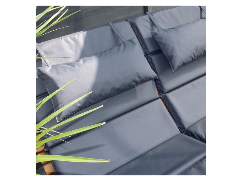 Sivé vankúše a podušky na drevenom ležadle so zelenými rastlinami.