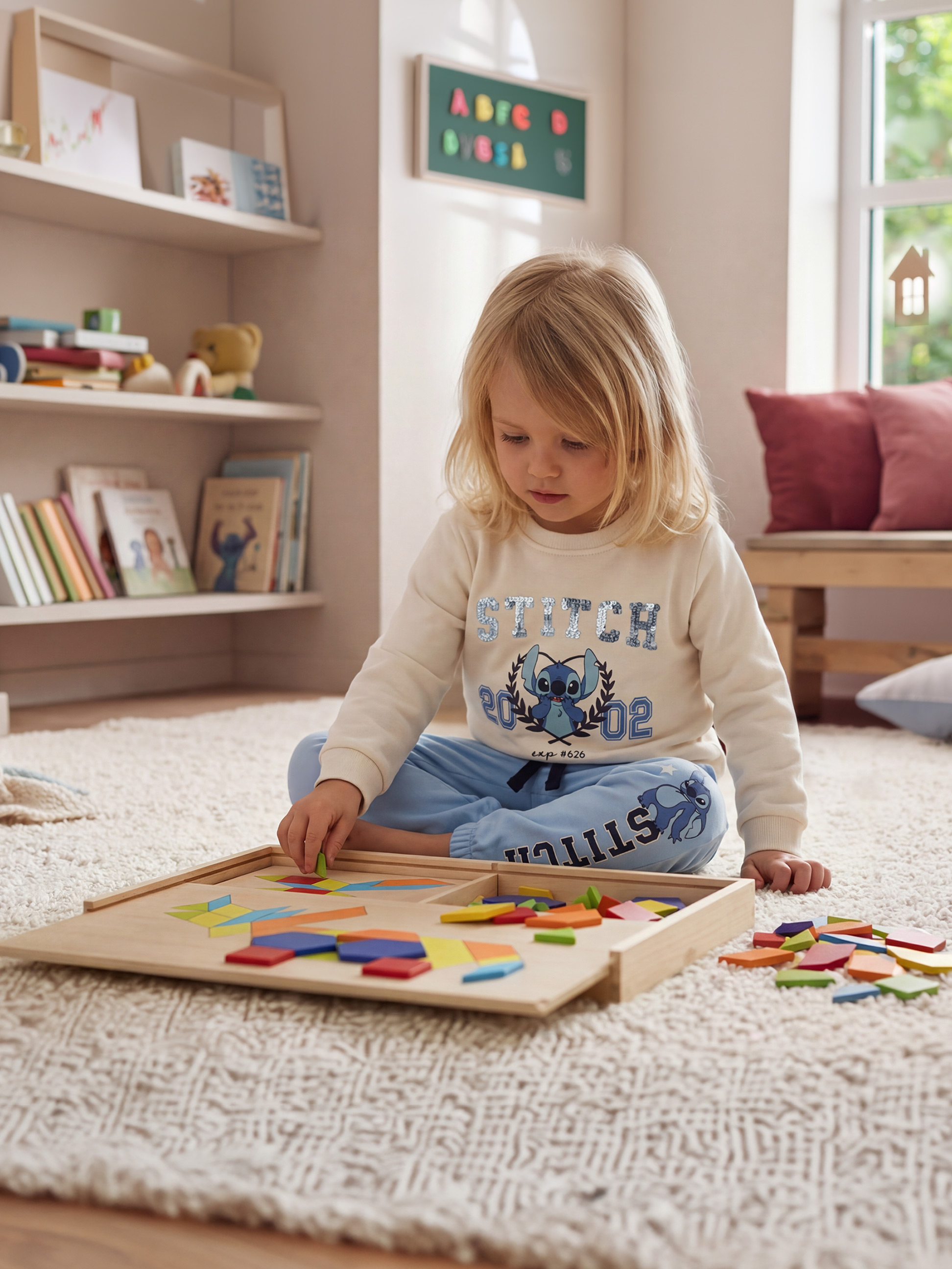 Dieťa sa hrá s farebným dreveným puzzle na huňatom koberci, oblečené v mikine a teplákoch.