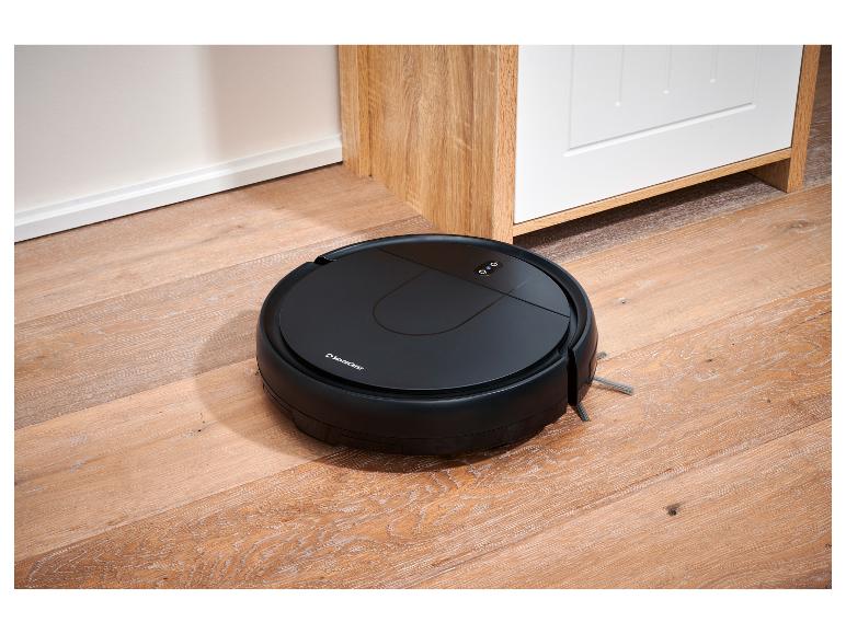 Robotický vysávač SilverCrest na drevenej podlahe vedľa bielej skrinky