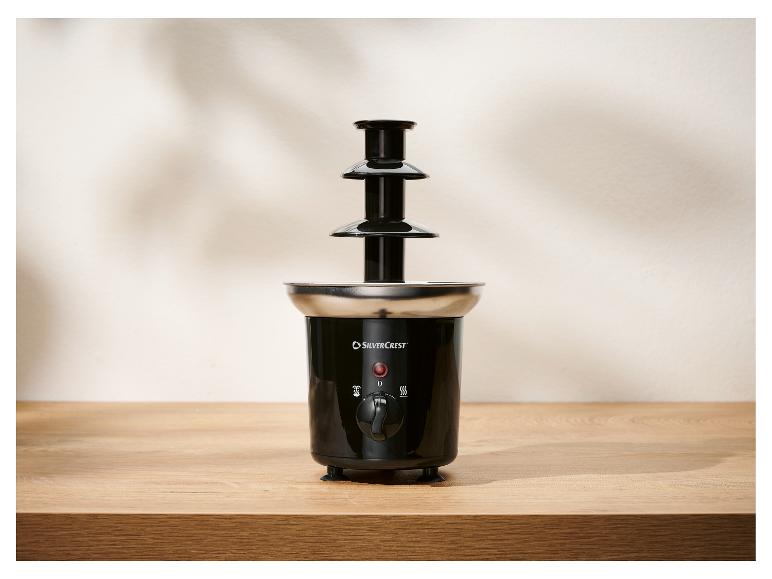 Čierna trojúrovňová čokoládová fontána s nerezovou základňou na drevenom stole.