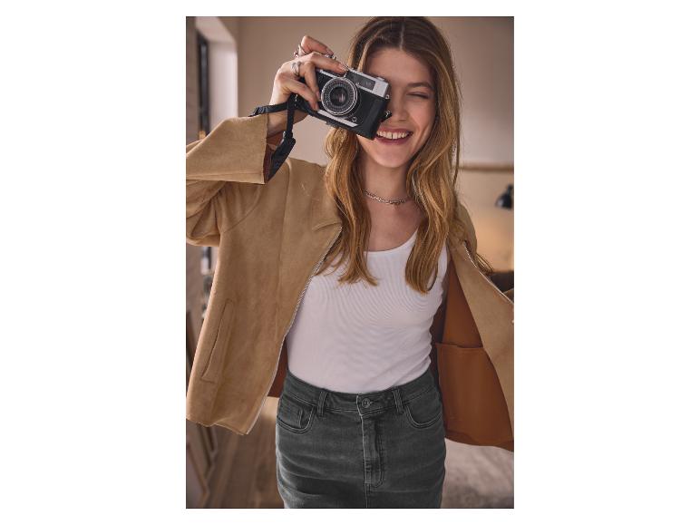 Žena v béžovej bunde a džínsovej sukni fotí starým fotoaparátom.