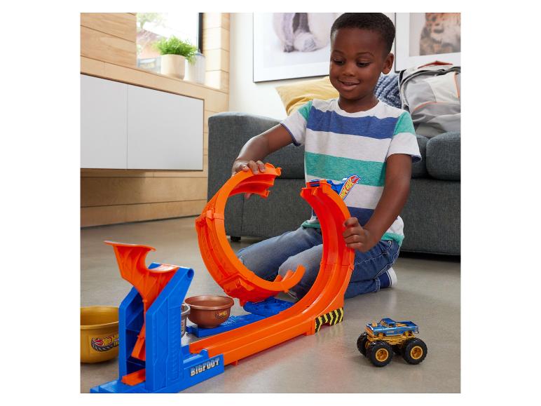 Usmiaty chlapec sa hrá so súpravou dráhy Hot Wheels Monster Trucks a autom.