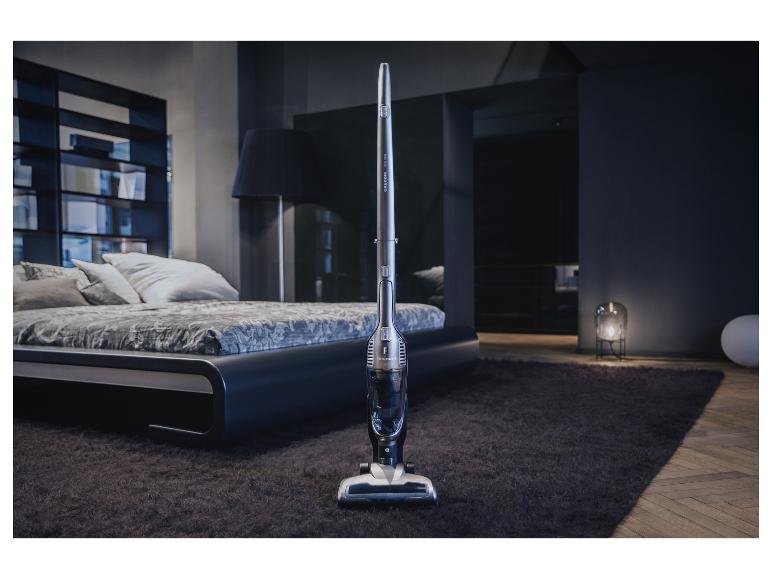 Tyčový vysávač Grundig v modernej spálni s posteľou a kobercom.