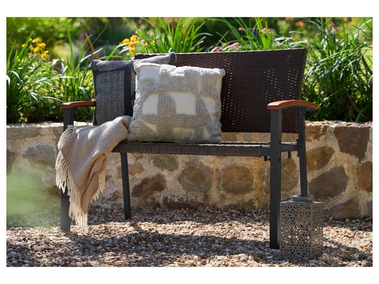 Záhradná lavička s vankúšmi a dekou, na pozadí zelene a kamenného múru.