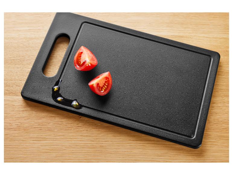 Dve polovice cherry paradajok na čiernej doske na krájanie s olejom