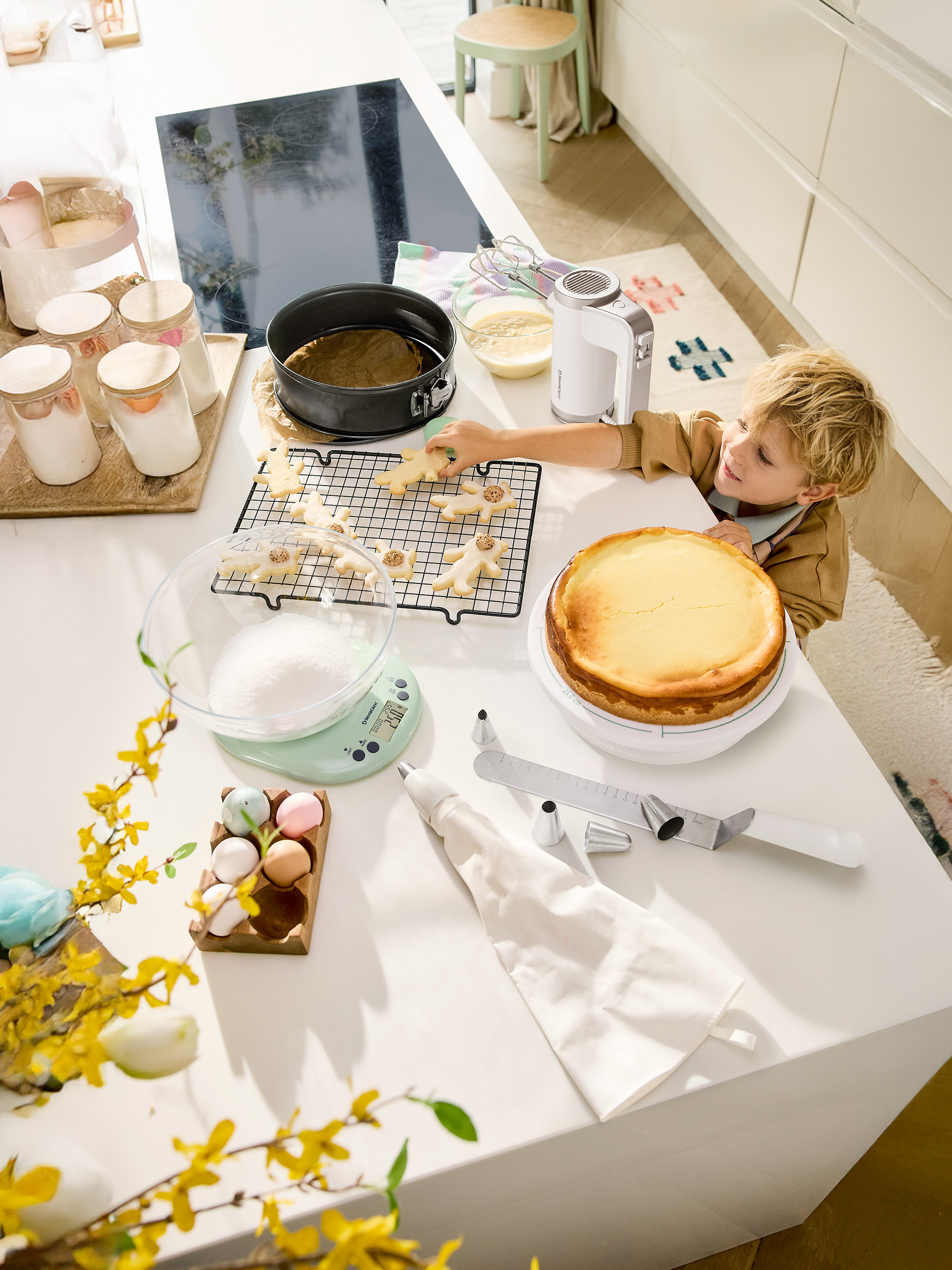 Dieťa zdobí veľkonočné sušienky a cheesecake na kuchynskej linke s nástrojmi na pečenie.