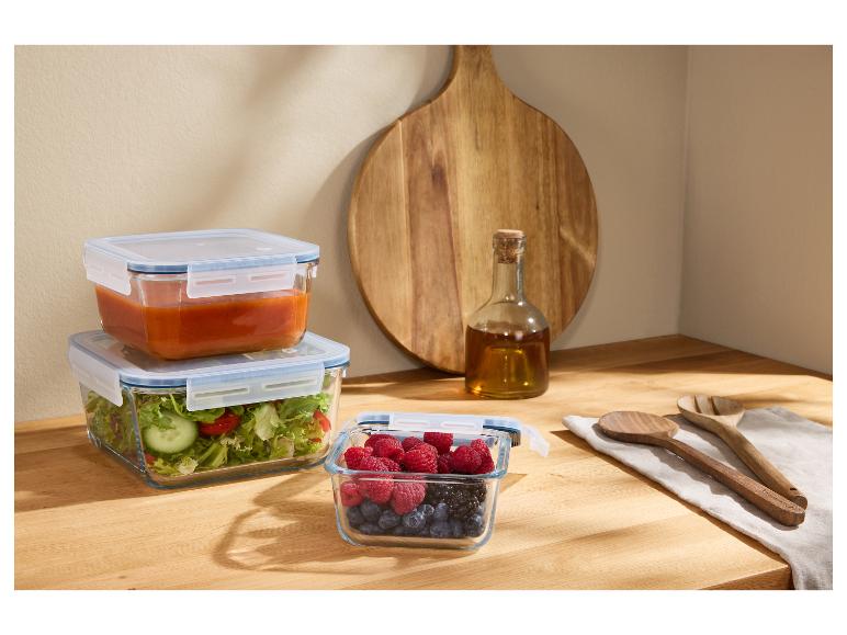 Sklenené nádoby s jedlom, drevená doska a fľaša oleja na drevenej doske.