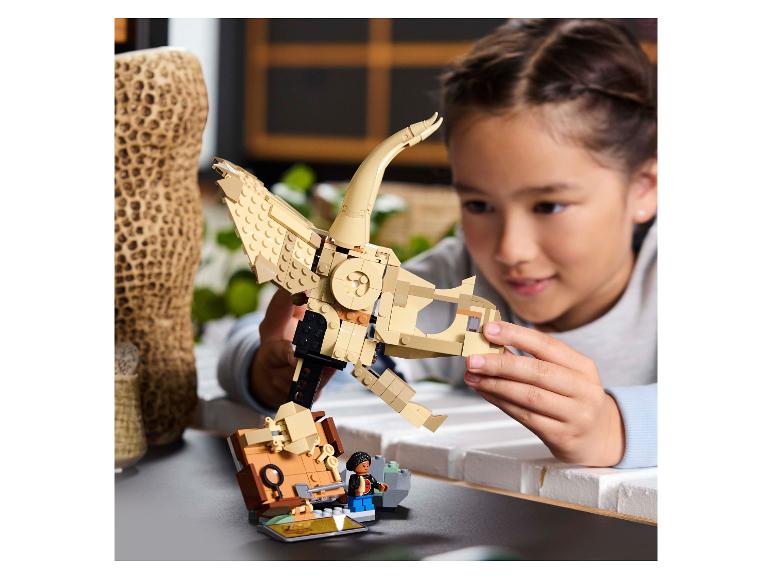 Dievča skladá LEGO kostru dinosaura, s LEGO minifigúrkou vedľa nej.