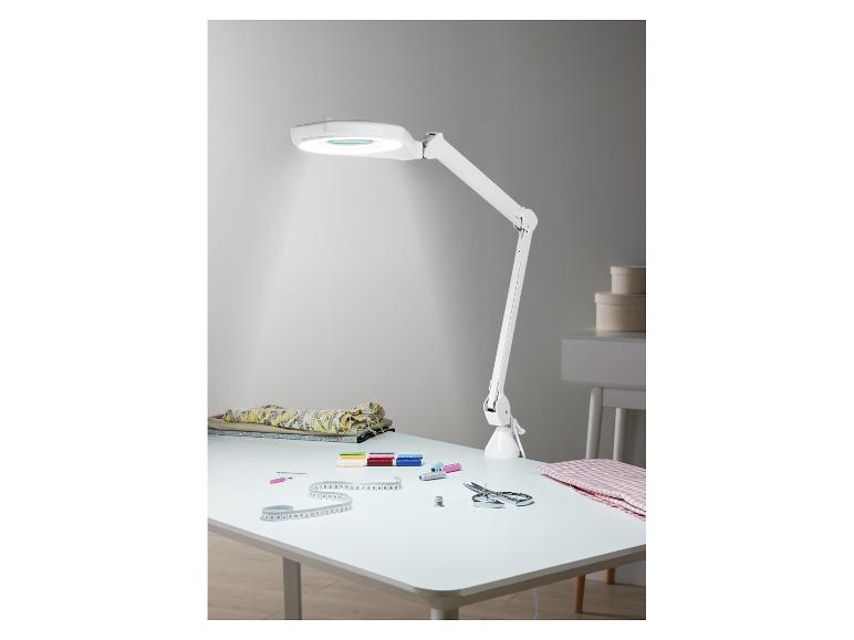 Biela stolová lampa s lupou a šijacími potrebami na bielom stole.