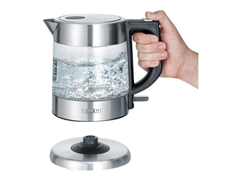 Sklenená rýchlovarná kanvica Severin s vriacou vodou, držaná rukou, vedľa základne.
